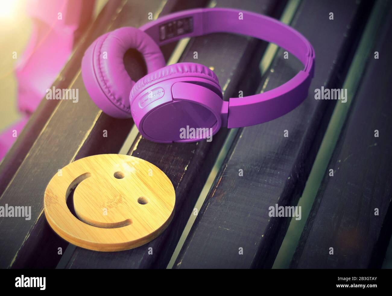 Fine music for perfect mood. Wireless headphones of purple color lie on a dark wooden bench. A wooden smile. The concept of love for music. No body. Stock Photo
