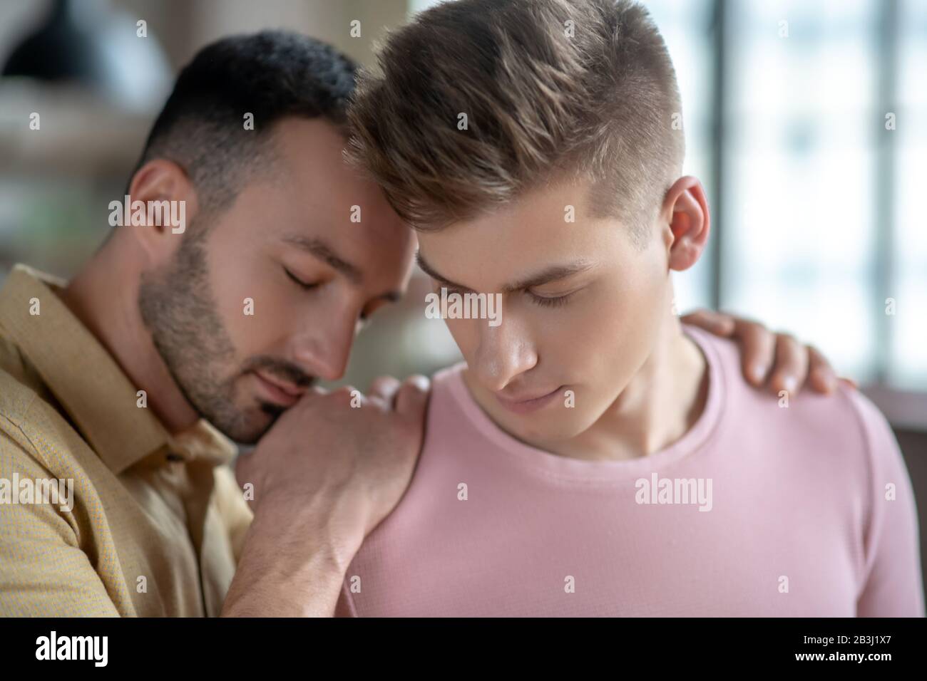 Dark-haired man in orange shirt putting hands on his partners shoulder ...