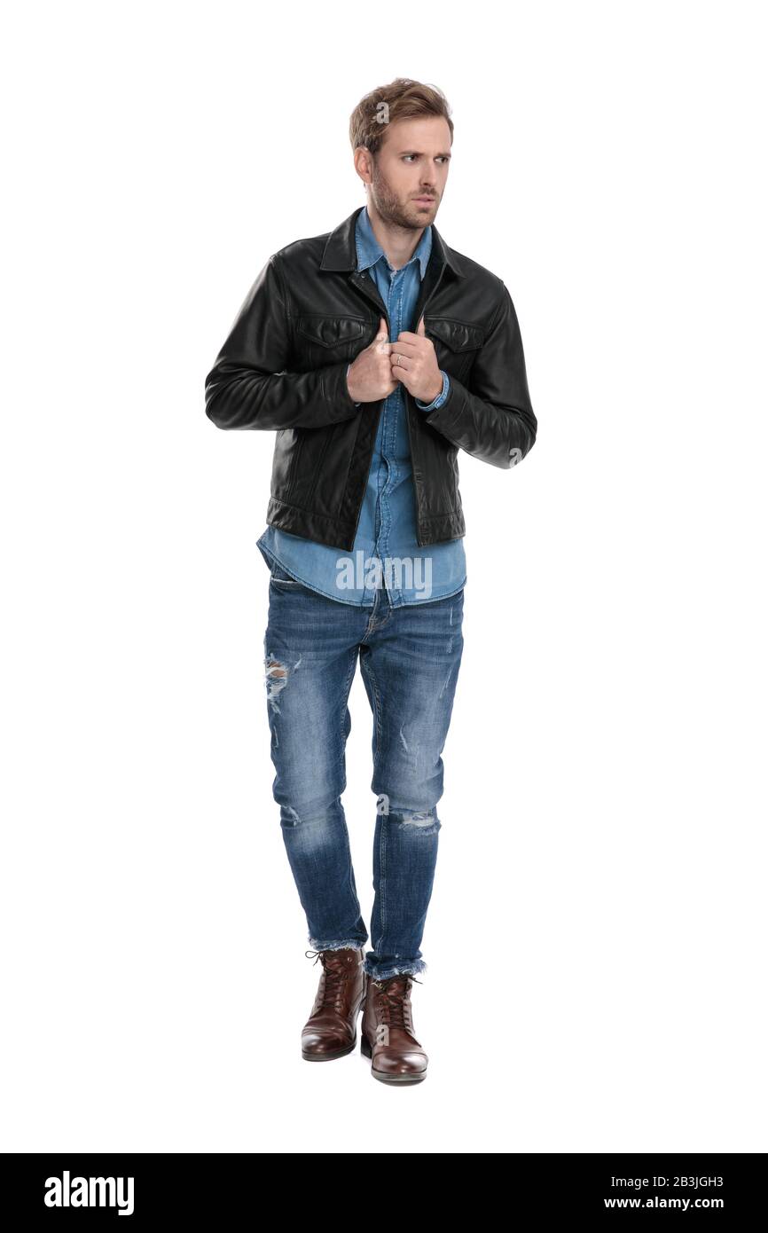 gorgeous casual man with black leather jacket is walking while fixing his jacket and looking away anxious  on white studio background Stock Photo