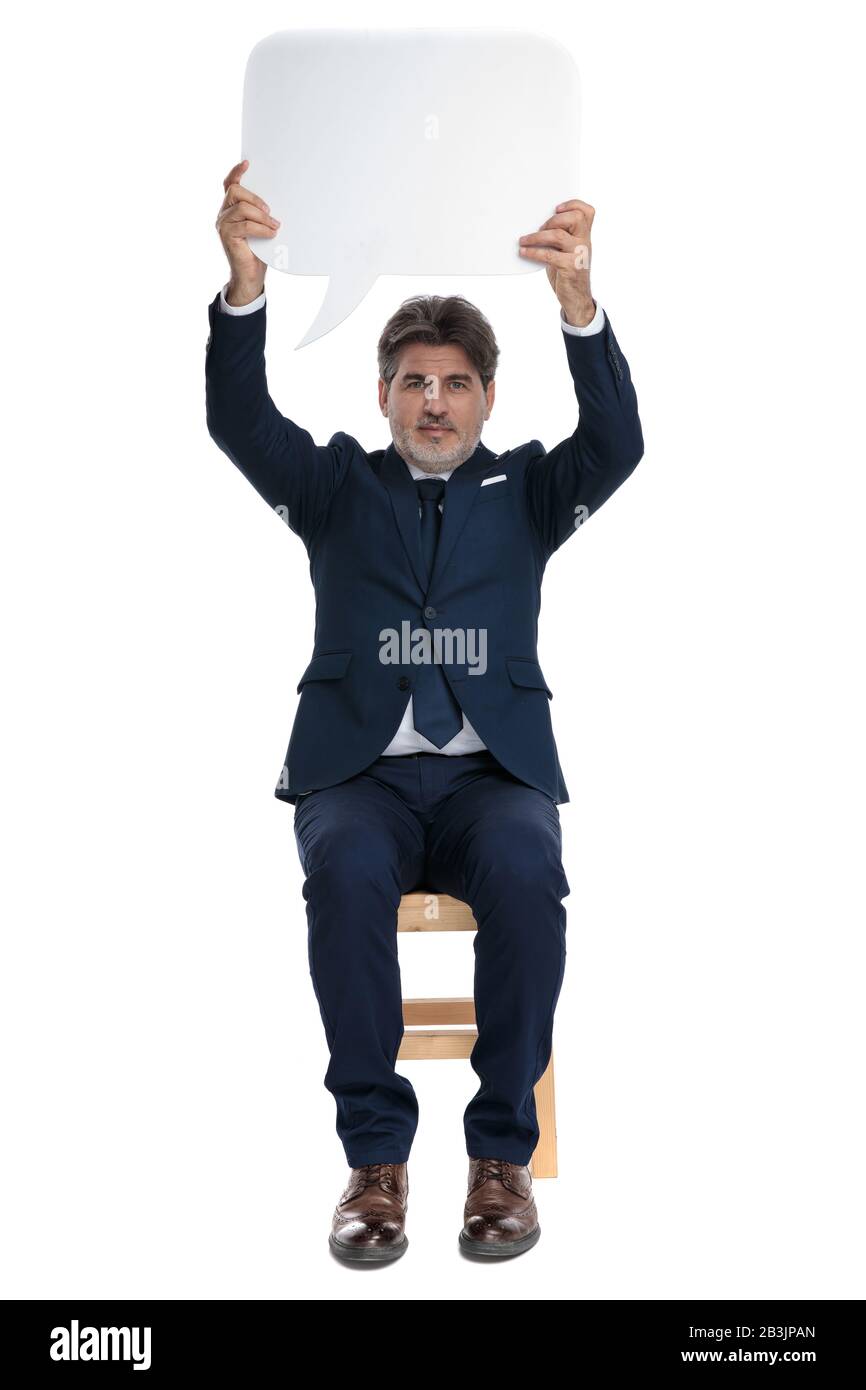 brown haired formal business man with navy suit is sitting and holding a speech bubble overhead serious Stock Photo