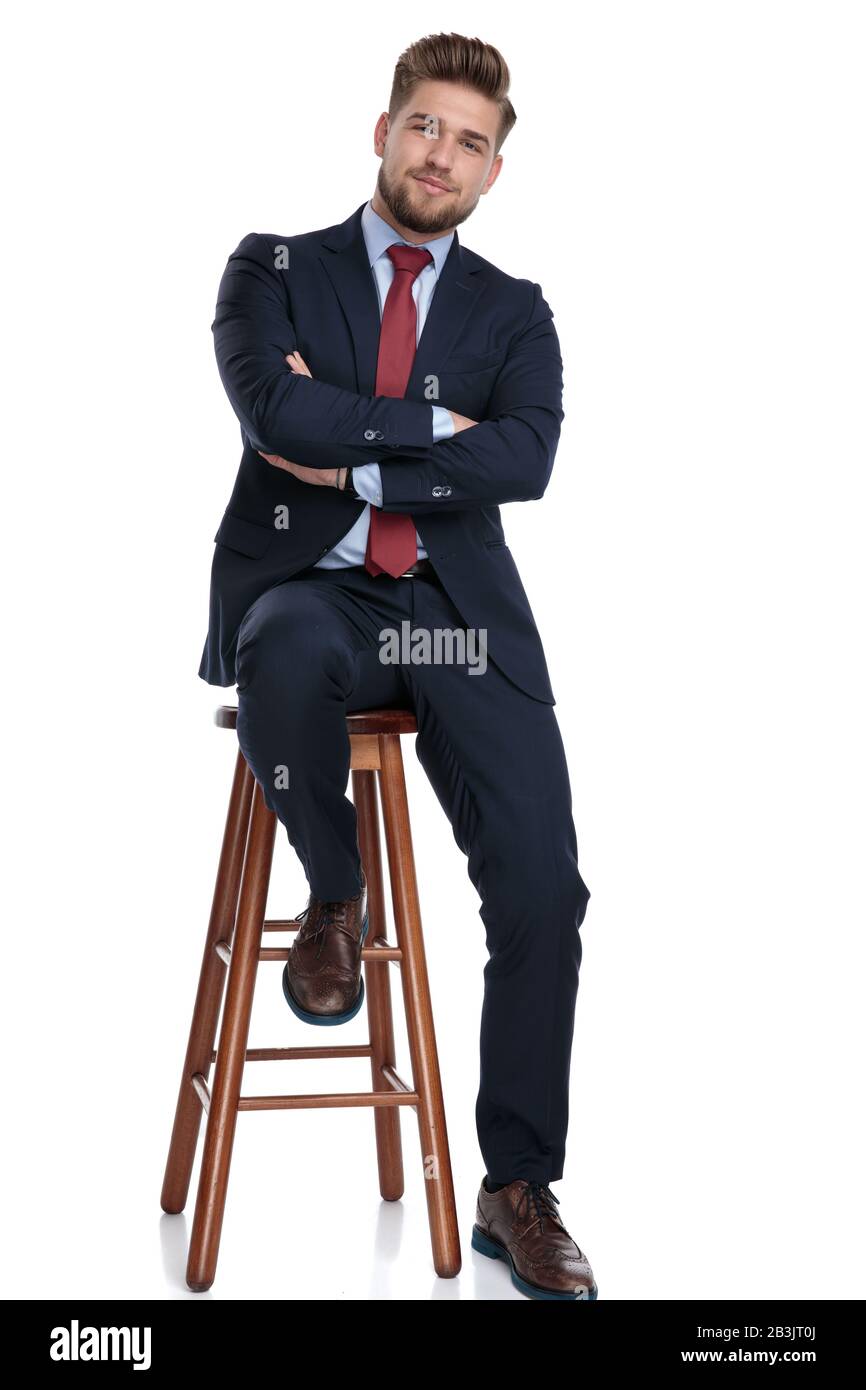 confident young businessman folding arms and sitting isolated on white background in studio Stock Photo