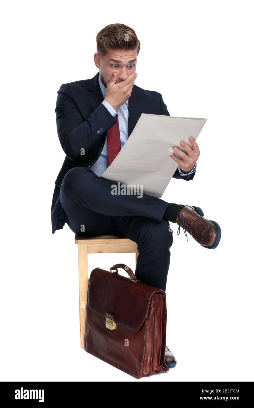 shocked young businessman reading newspaper and covering his mouth with ...