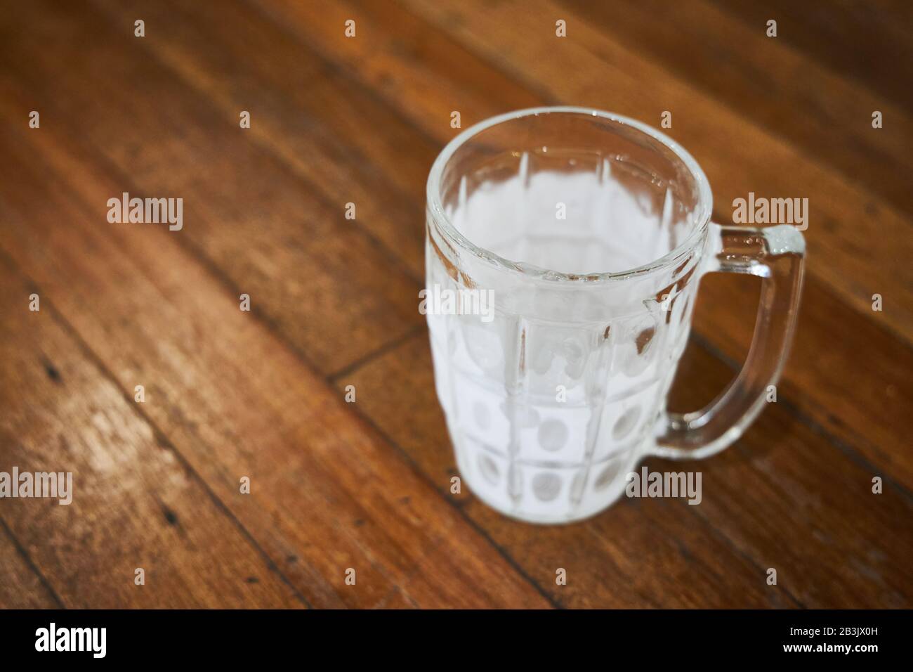 An empty mug for beer covered with hoarfrost stands on a wooden table of a pub. Stock Photo