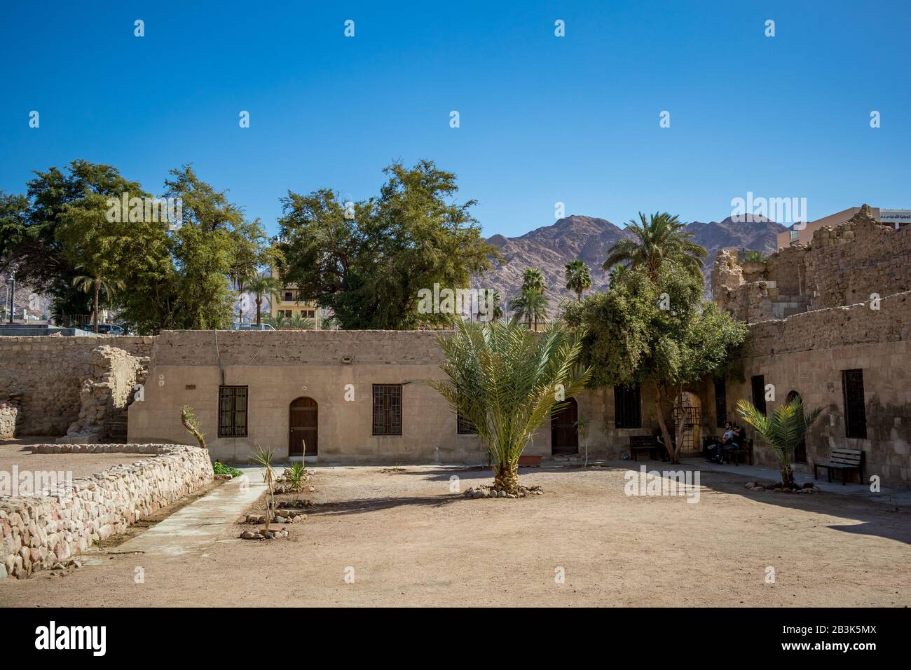 AQABA, JORDAN - JANUARY 31, 2020: Tourists rest under fortress walls shadows. Court yard view of Aqaba Castle. Main fort square is empty under the sunlight. Sunny winter day. Clear cloudless blue sky Stock Photo
