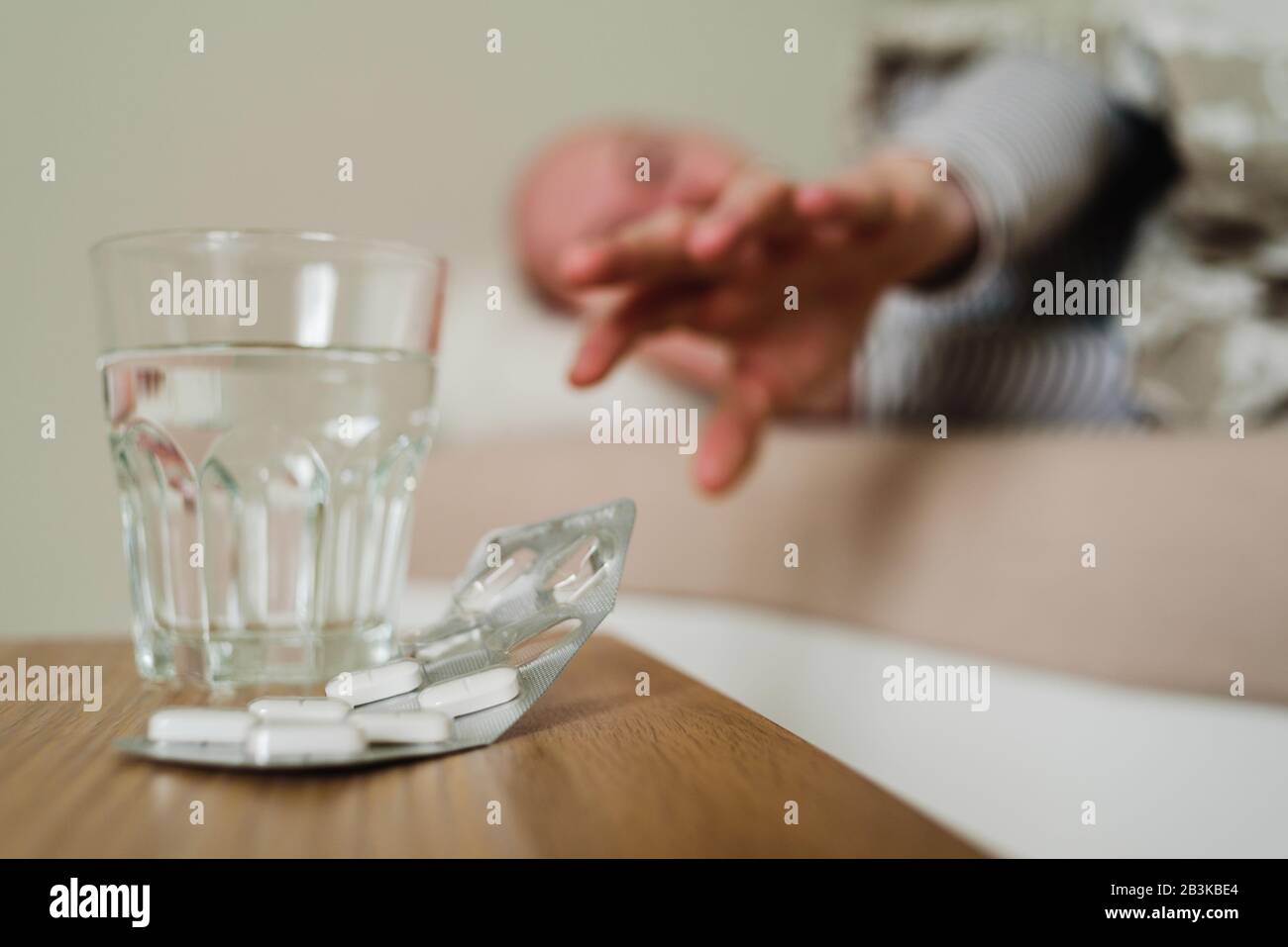 Sick man lying in bed with pills and glass of water on foreground. Pulling  his hand for a glass or tablets Stock Photo - Alamy