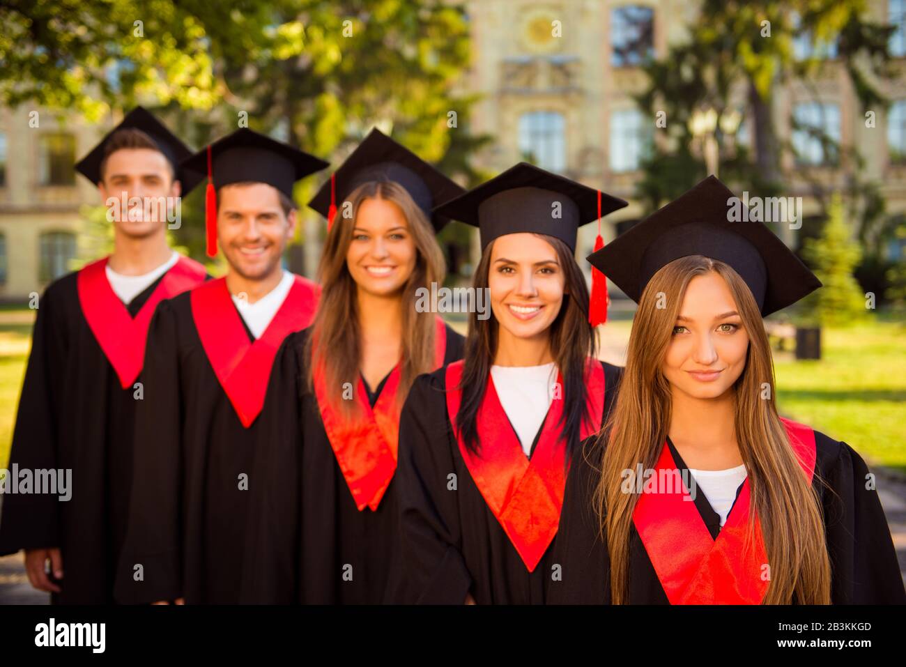 successful confident five graduates in robes and hats with tassel smiling Stock Photo