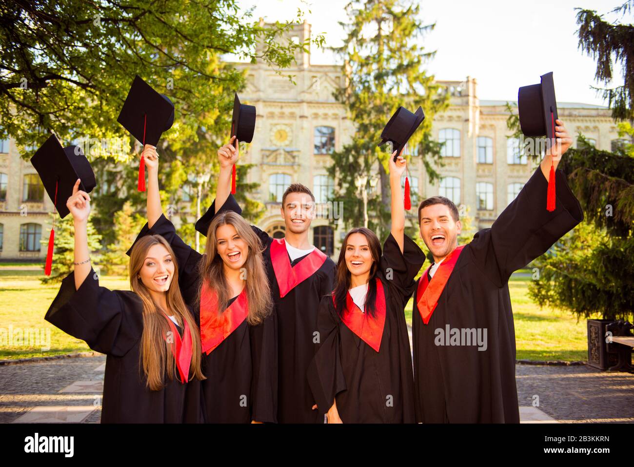 excited successful happy five graduates in robes together rise mortar-board with tassel Stock Photo