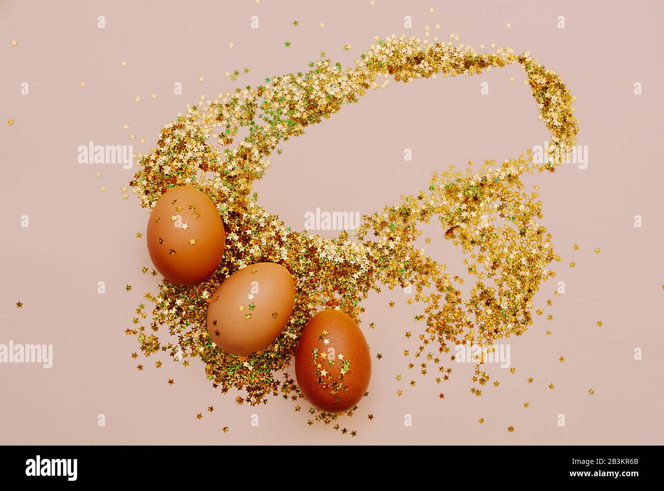 Easter holiday brown eggs in a large pile of shiny gold stars on a delicate pink background. Easter layout in art Deco style Stock Photo