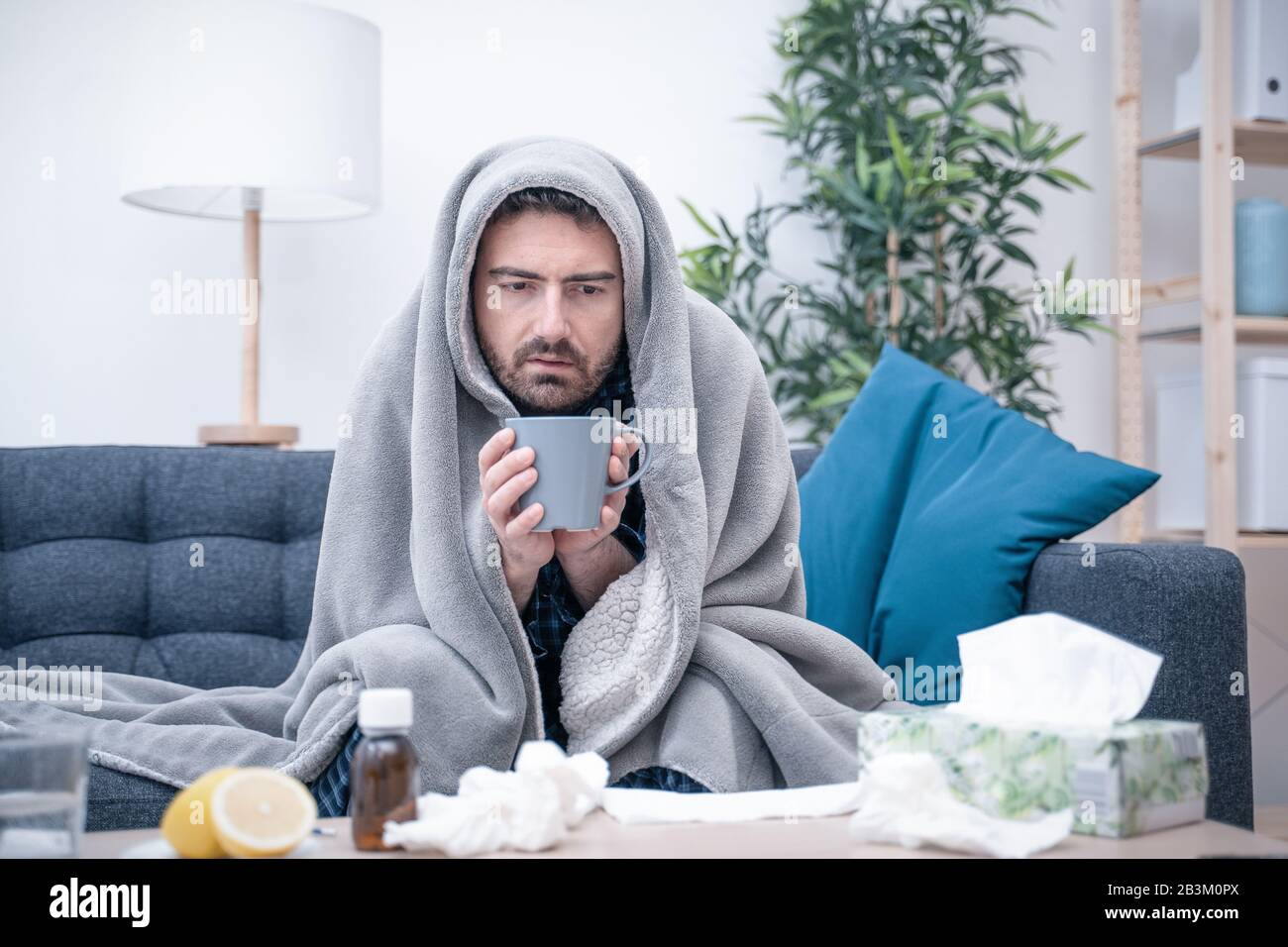Man wrapped in plaid lying on the sofa feeling sick illness at home Stock  Photo - Alamy