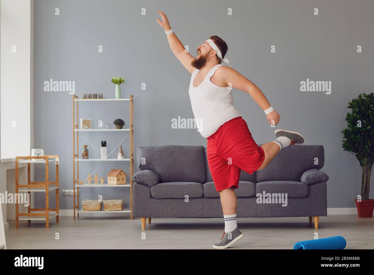Funny red fat man doing exercises while standing at home. Stock Photo