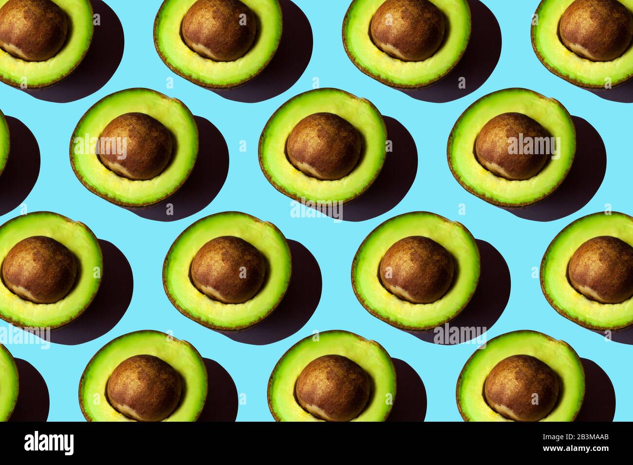 Half avocado, pattern on blue backdrop. keto diet food photo. Fresh fruit. Stock Photo