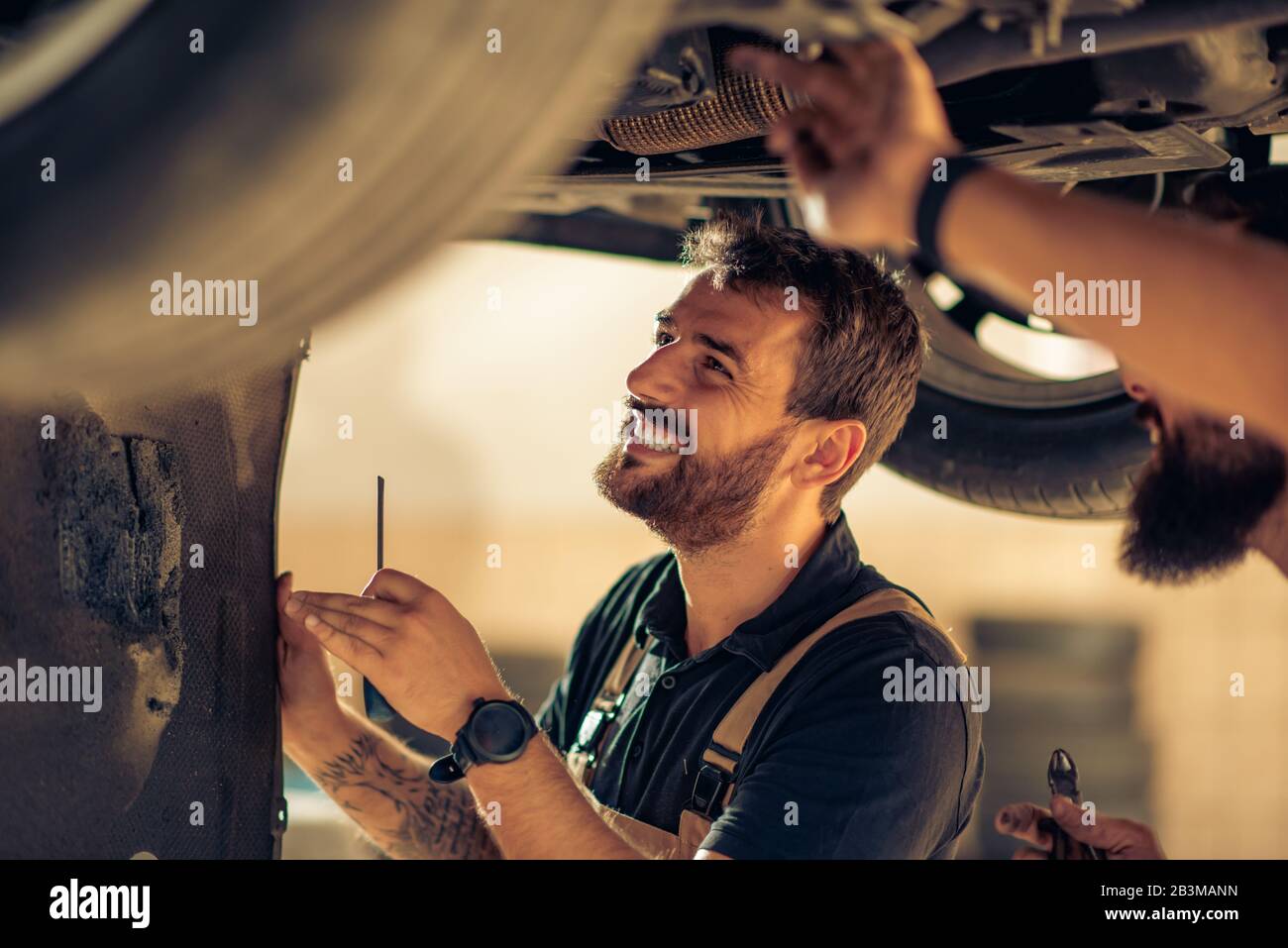 Workcomp Mechanic Car mechanic ready for work.Young mechanic examining car suspension at ...