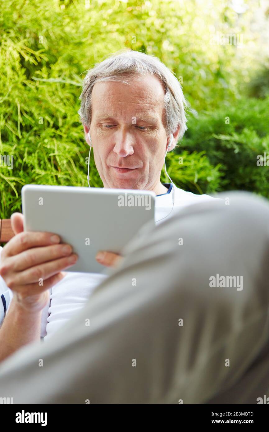 Old man with tablet computer and headphones watches a movie Stock Photo