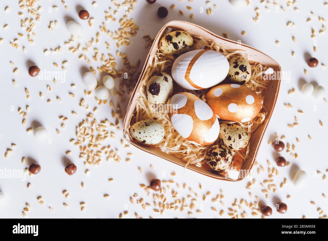 Assorted gold Easter eggs, chocolate dragee candies and millet in a basket  on a white background Stock Photo - Alamy