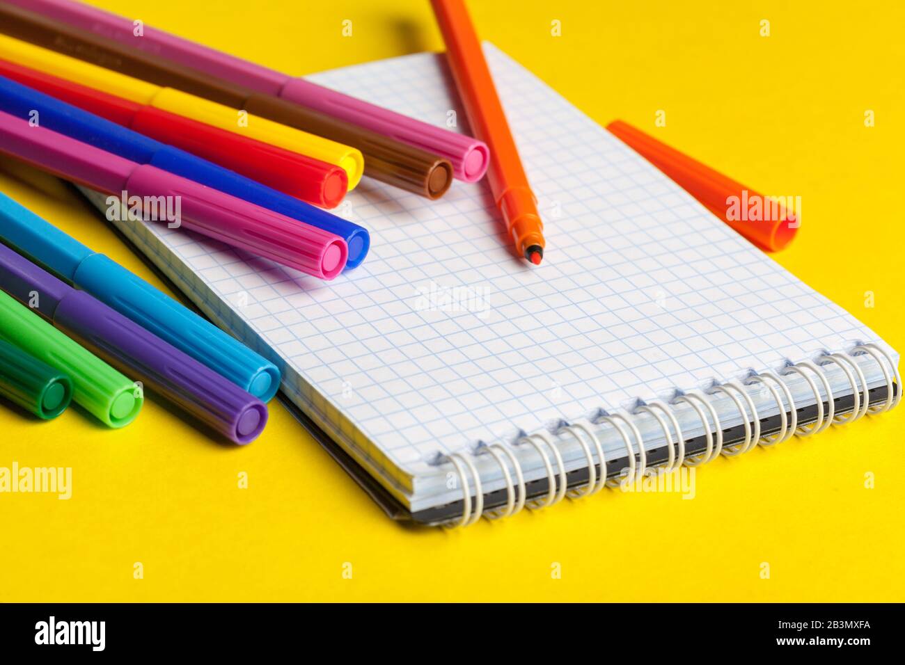 Felt-tip pens and blank notepad on bright yellow background Stock Photo