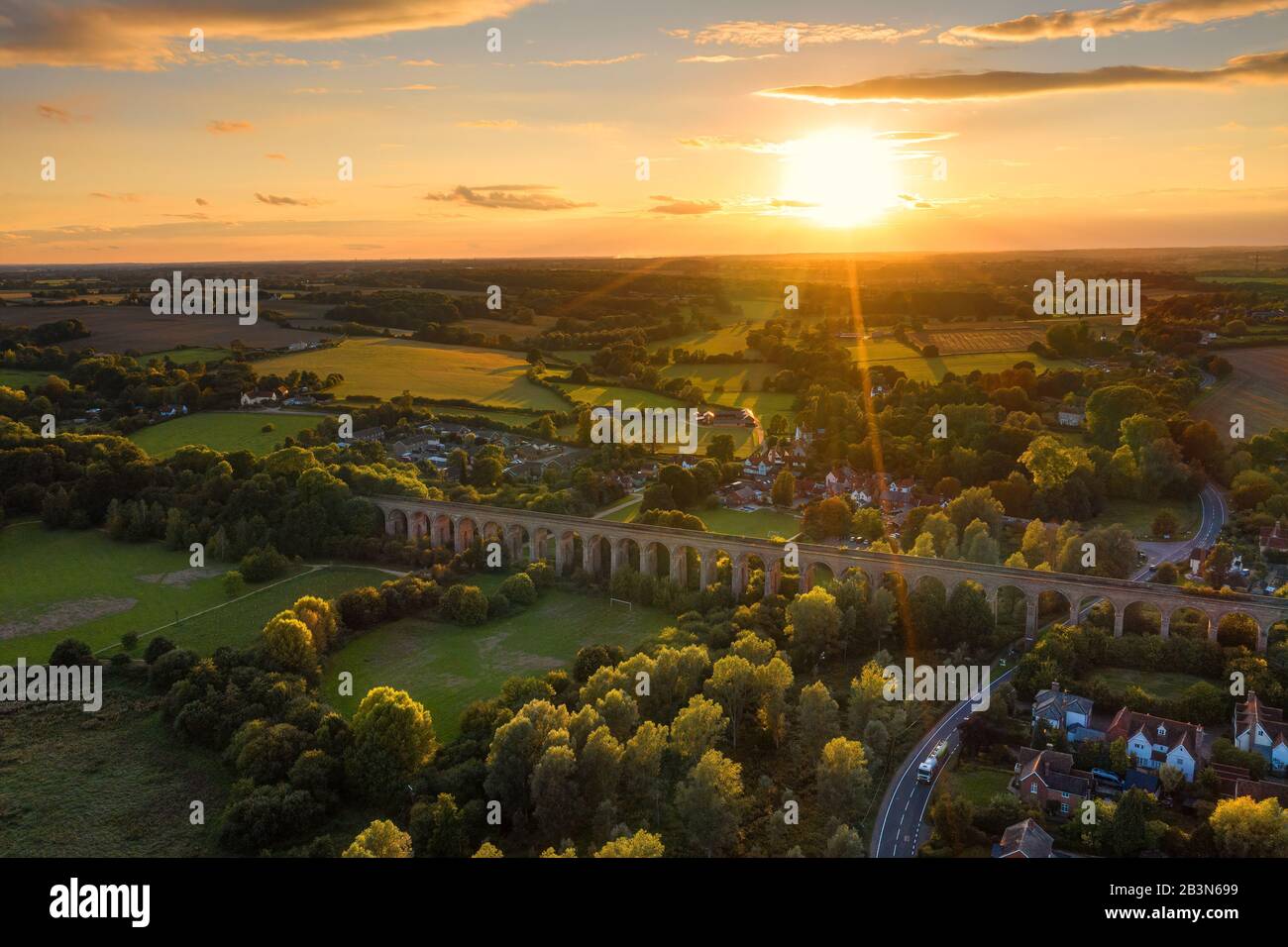 The railway viaduct at Chappel and Wakes Colne in Essex, England the sun a gold ball just above the horizon casting rays light and shadows Stock Photo