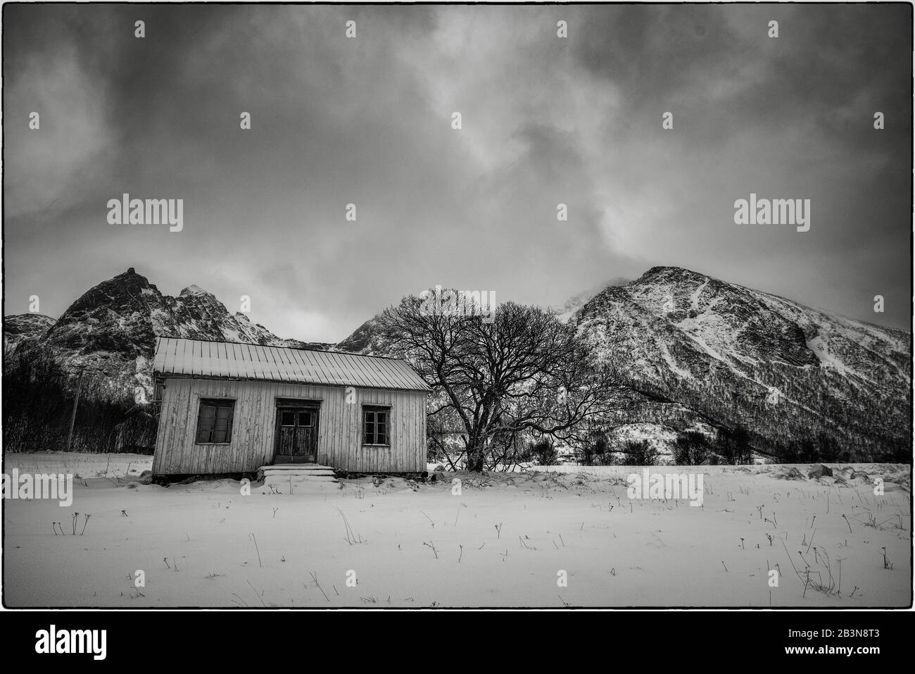 Black and white photo of a house (door and 2 windows), tree and mountains in Norway reminding of a child's drawing Stock Photo