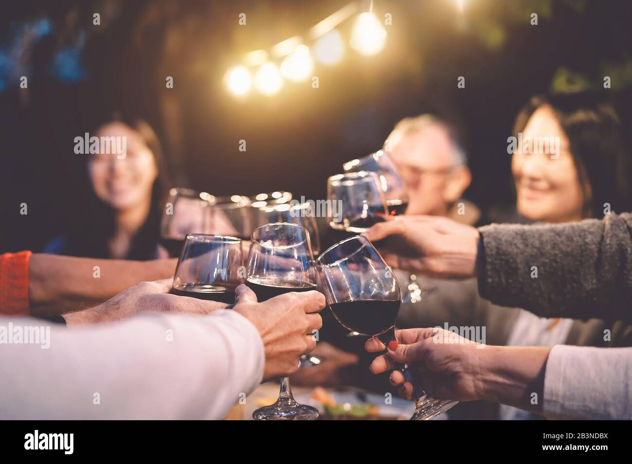 Happy family cheering with red wine at reunion dinner in garden - Senior having fun toasting wineglasses and dining together outdoor Stock Photo