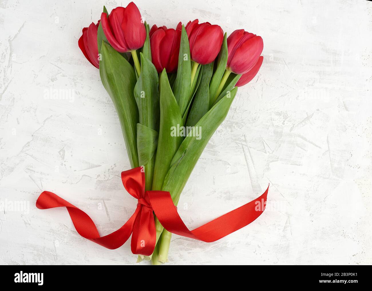 bouquet of red blooming tulips with green stems and leaves on a white ...