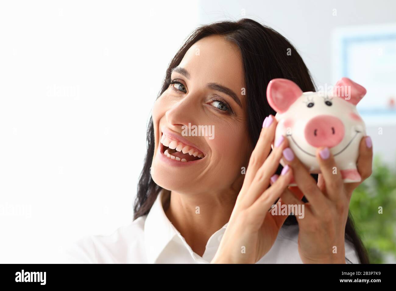Beautiful woman shows piggy bank and smiles Stock Photo - Alamy