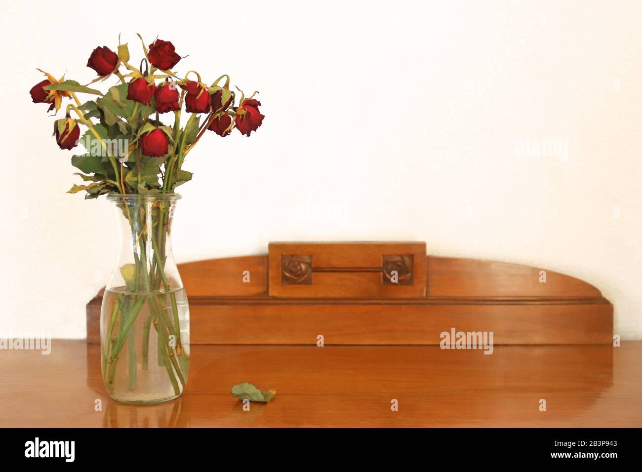 vase with withered red roses standing on an old wooden sideboard Stock Photo