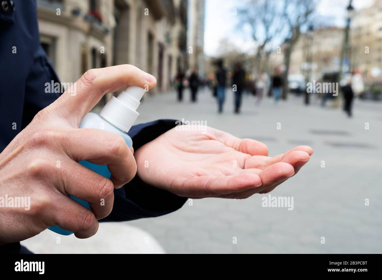 closeup of a caucasian man on the street disinfecting his hands with a blue hand sanitizer from a bottle Stock Photo