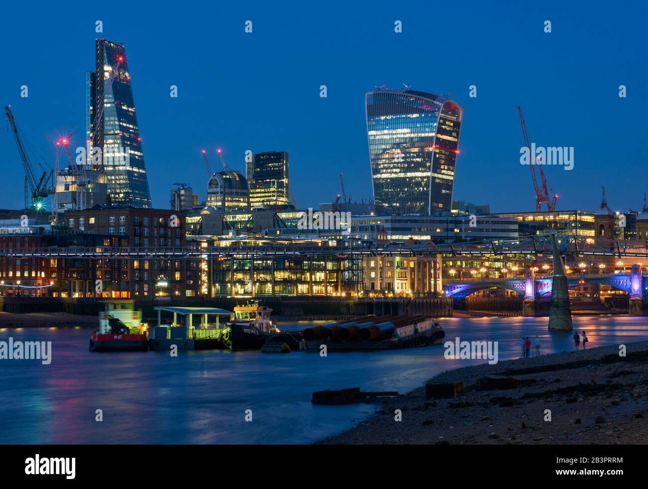City of London buildings at night, viewed from the South Bank, with the Millennium Bridge and the Walkie Talkie Tower Stock Photo