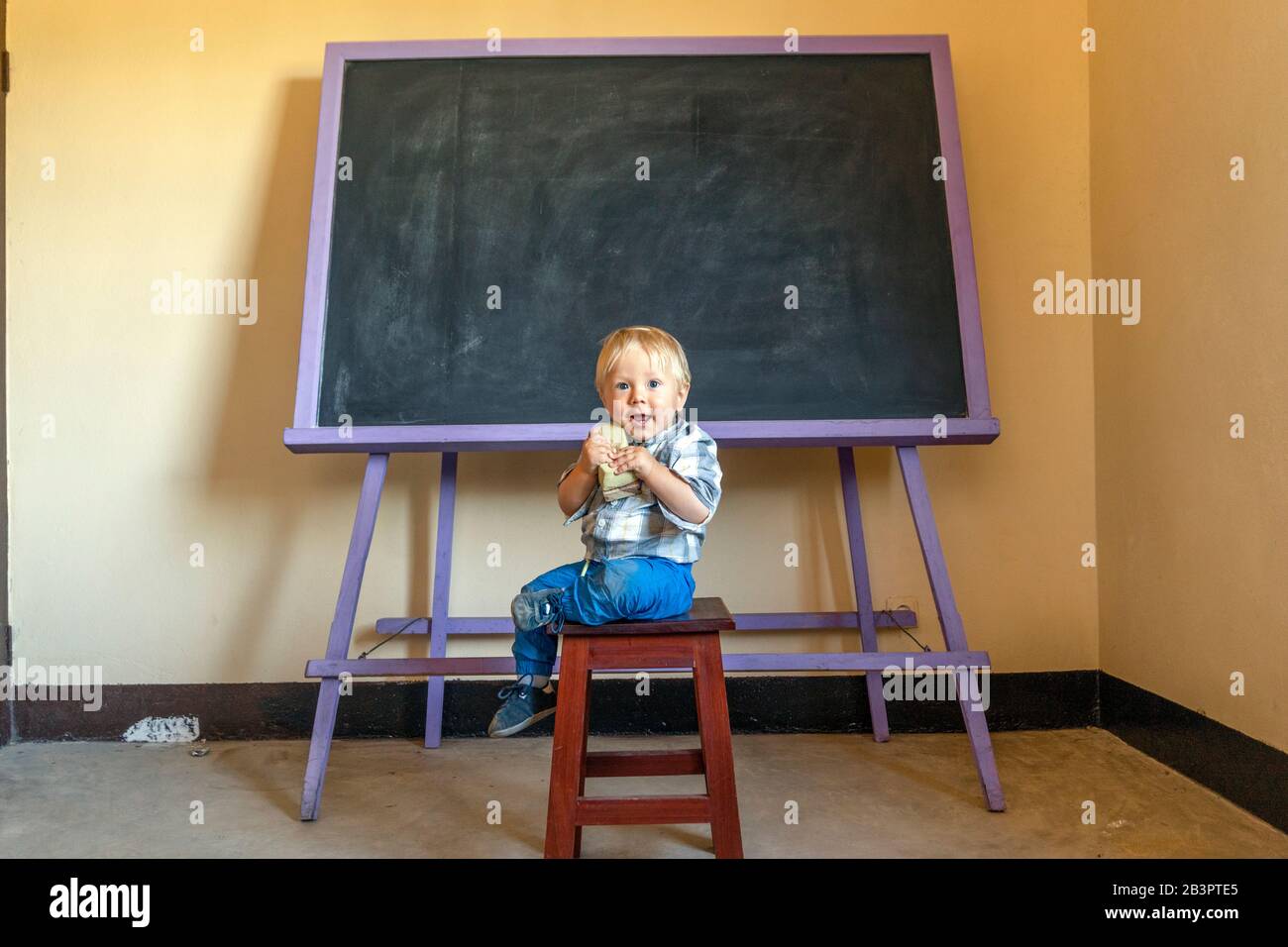 Cute blonde boy sitting with a board sponge by vintage blackboard Stock Photo