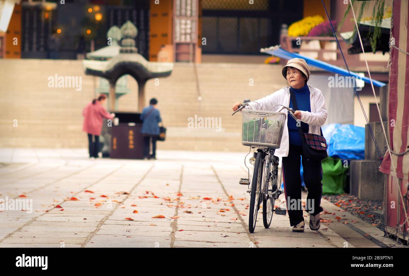 TOKYO, JAPAN - NOVEMBER 25, 2019: Local Japanese lady with bicycle finishes her praying in a temple Stock Photo