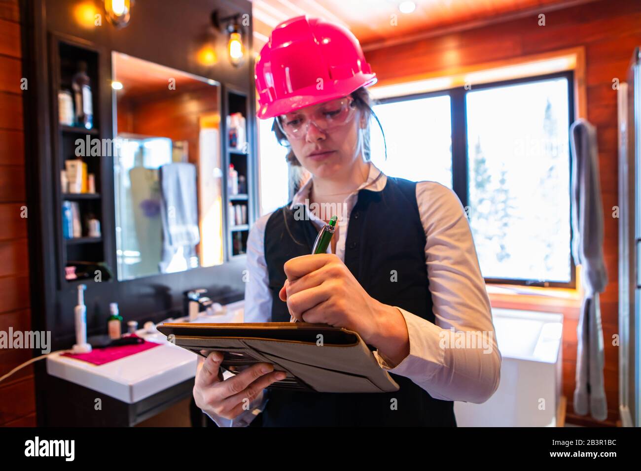female home inspector wearing a pink hard hat. she taking notes with