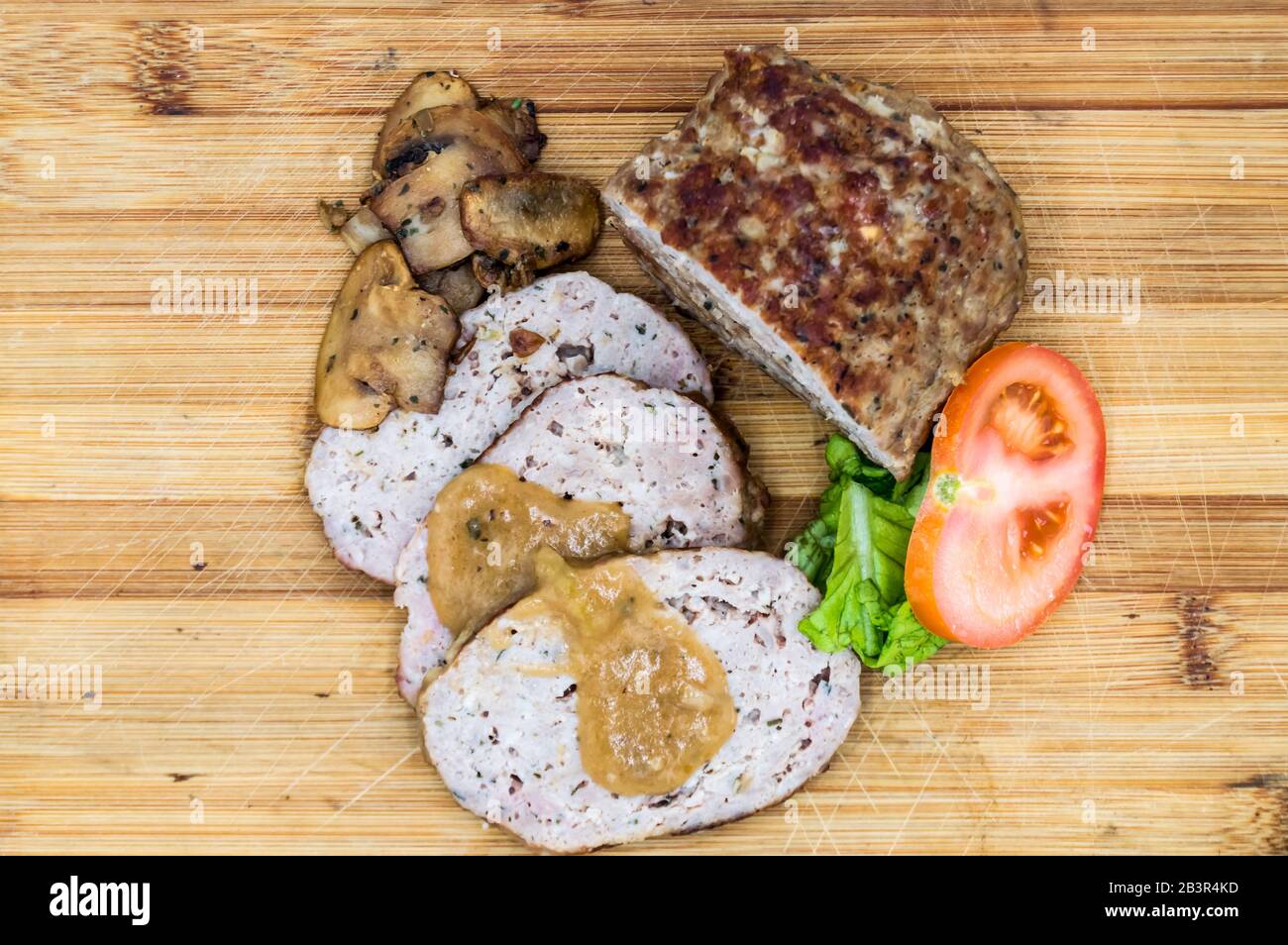 Meatloaf cut into slices with mushrooms, tomato and salad top view on an isolated wooden background. Stock Photo