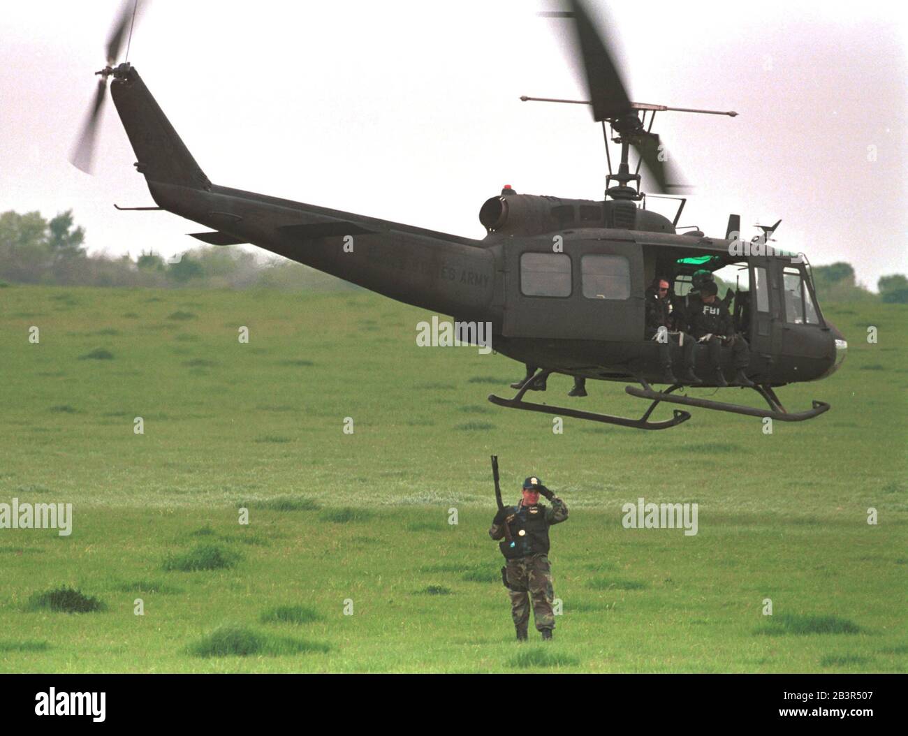 Waco Texas March 1993: A U.S. Army helicopter with FBI agents aboard flies over a field near the Branch Davidian compound near Waco as an Alcohol Firearms and Tobacco (ATF) agent stands below with a loaded weapon during the 51-day standoff  between members of the religious sect and federal law enforcement agents. The siege ended April 18 when fire swept through the compound, killing 76 people. ©Bob Daemmrich Stock Photo