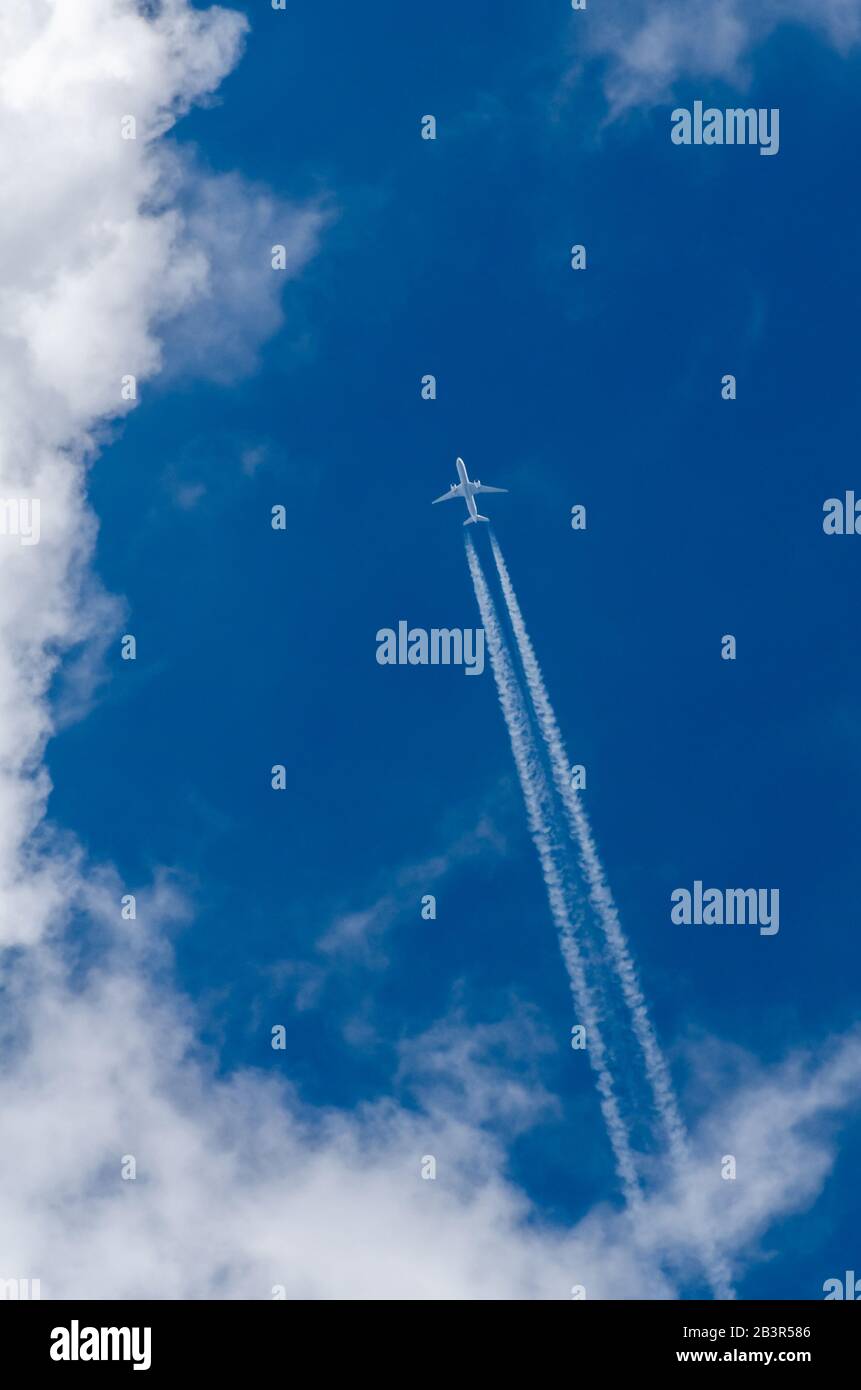 Twin jet commercial passenger aircraft flying directly above against blue sky with clouds and condensation trails over Germany, Western Europe Stock Photo