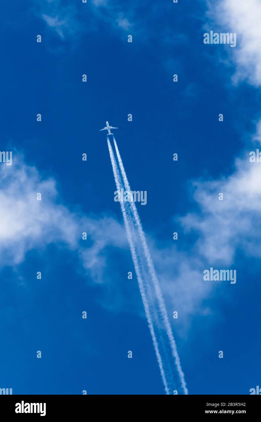 Twin jet commercial passenger aircraft flying directly above against blue sky with clouds and condensation trails over Germany, Western Europe Stock Photo