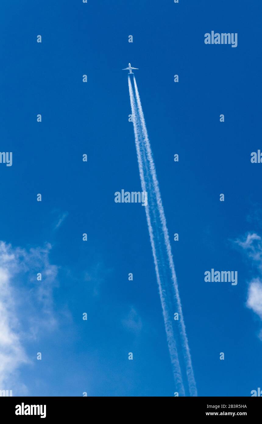 Twin jet commercial passenger aircraft flying directly above against blue sky with clouds and condensation trails over Germany, Western Europe Stock Photo