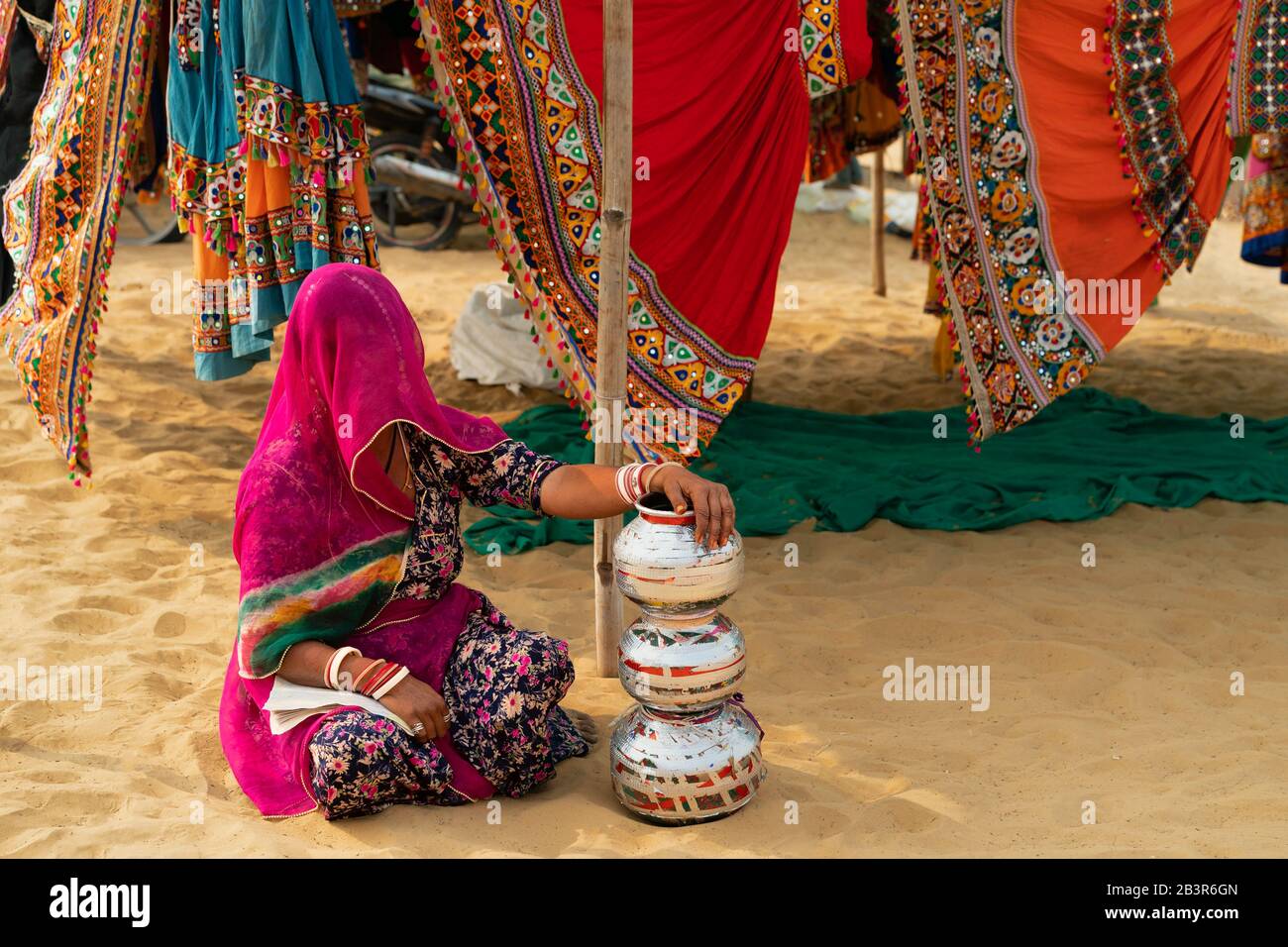 Woman under veil and with traditional clothes selling colorful skirts in desert near Pushkar, Rajasthan, India. Stock Photo