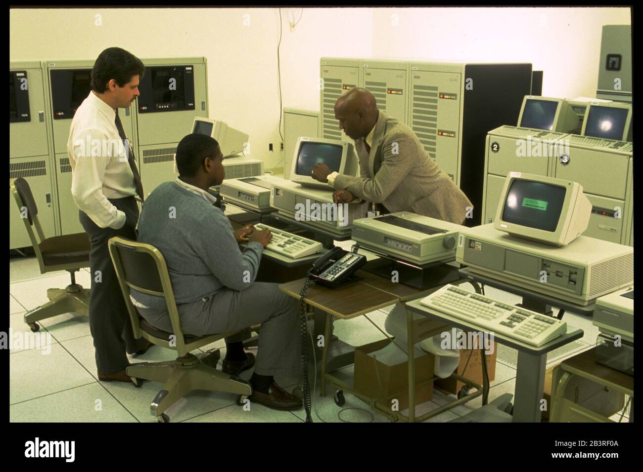 Austin Texas USA,1990: Supervisor watches data entry specialist work on computer terminal with mainframe computers in the background at a processing c Stock Photo
