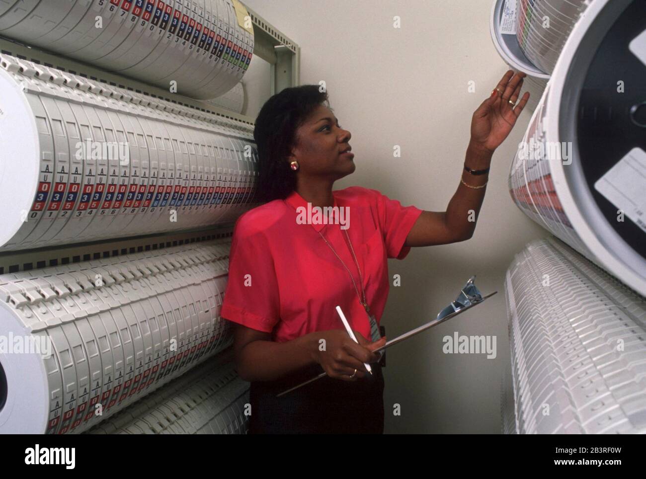 Austin Texas USA, 1990: Black female clerk looks at racks of magnetic tapes storing data compiled at the United States Census regional data processing center. ©Bob Daemmrich Stock Photo