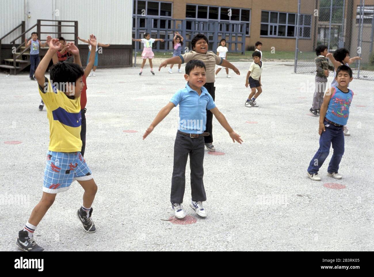 San Antonio, Texas USA, circa 1992: Texas school funding crisis-- Elementary school students do jumping jacks on a poorly maintained asphalt surface during physical education class at Frey School in the chronically underfunded Edgewood School District. ©Bob Daemmrich Stock Photo