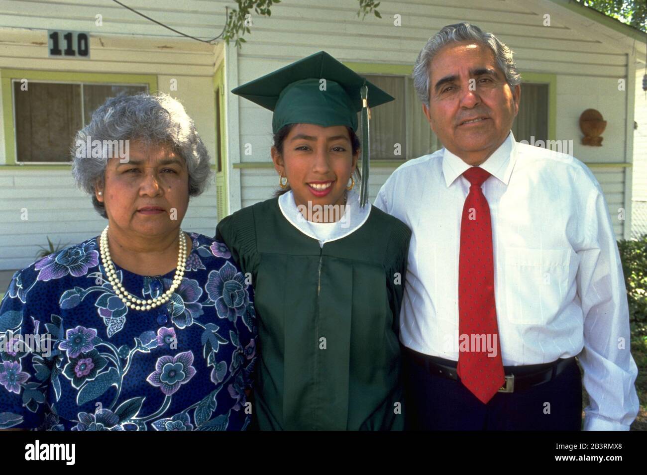 San Antonio Texas USA, circa 1990: Female high school senior wearing cap and gown gets kiss from her father at home before her commencement ceremony from Edgewood High School. Her father, Demetrio Rodriguez, is the named plaintiff in Rodriguez v. San Antonio Independent School District, which led to the landmark Edgewood v. Kirby lawsuit that forced the state of Texas to make its funding of public schools more equitable between districts serving rich and white students and those serving poor and minority students.  MR ES-0122 Model Released  ©Bob Daemmrich Stock Photo