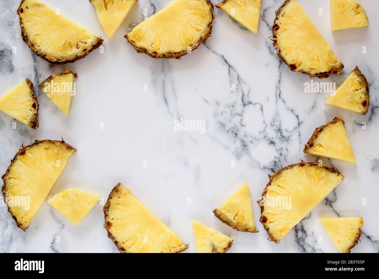 Pineapple slices on a white marble background with a copy space in the middle Stock Photo
