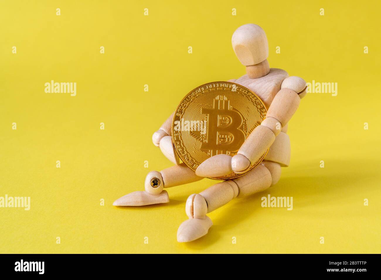Wooden doll tightly holding Bitcoin while sitting on yellow background  Stock Photo - Alamy