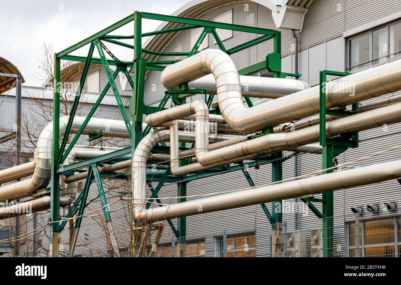 Complex pipeline of a power plant. Multiple aluminium pipes entangled with each other and supported by a green metal frame. Stock Photo