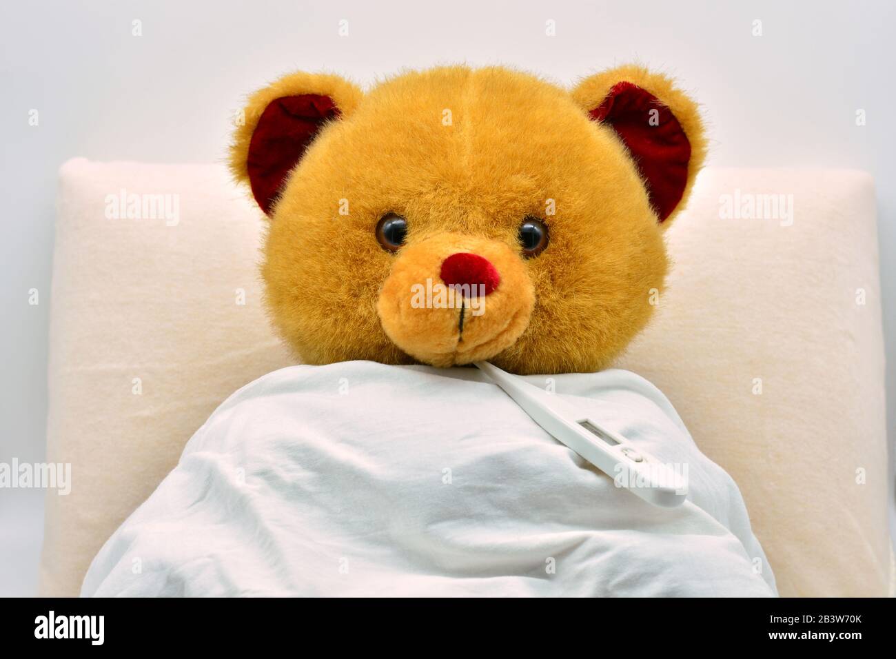 Teddy bear in bed, sick, with thermometer put in mouth Stock Photo