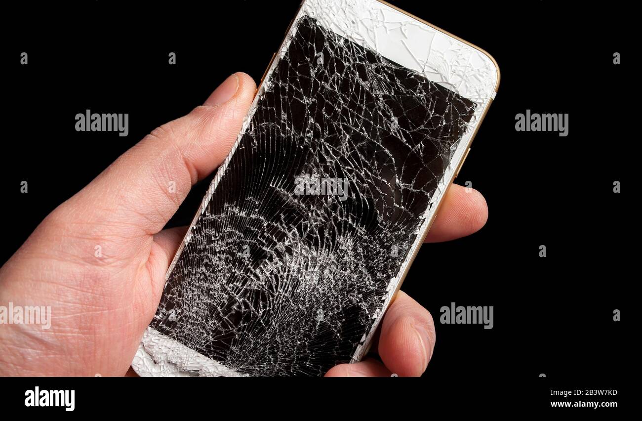 Modern smartphone with highly broken screen in men hand on black background. Stock Photo