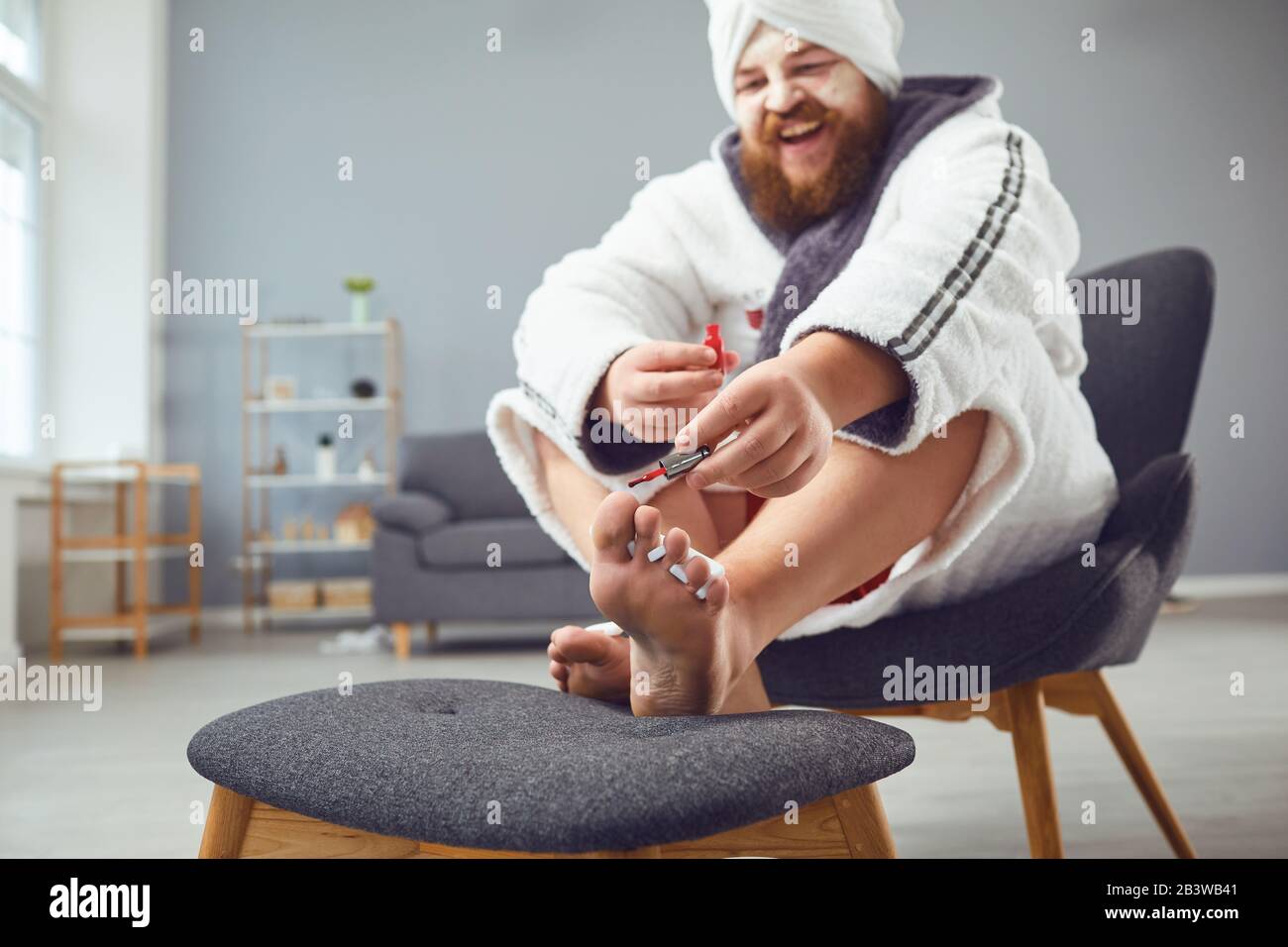 Funny pedicure concept. Funny fat man in a bathrobe and a towel paints