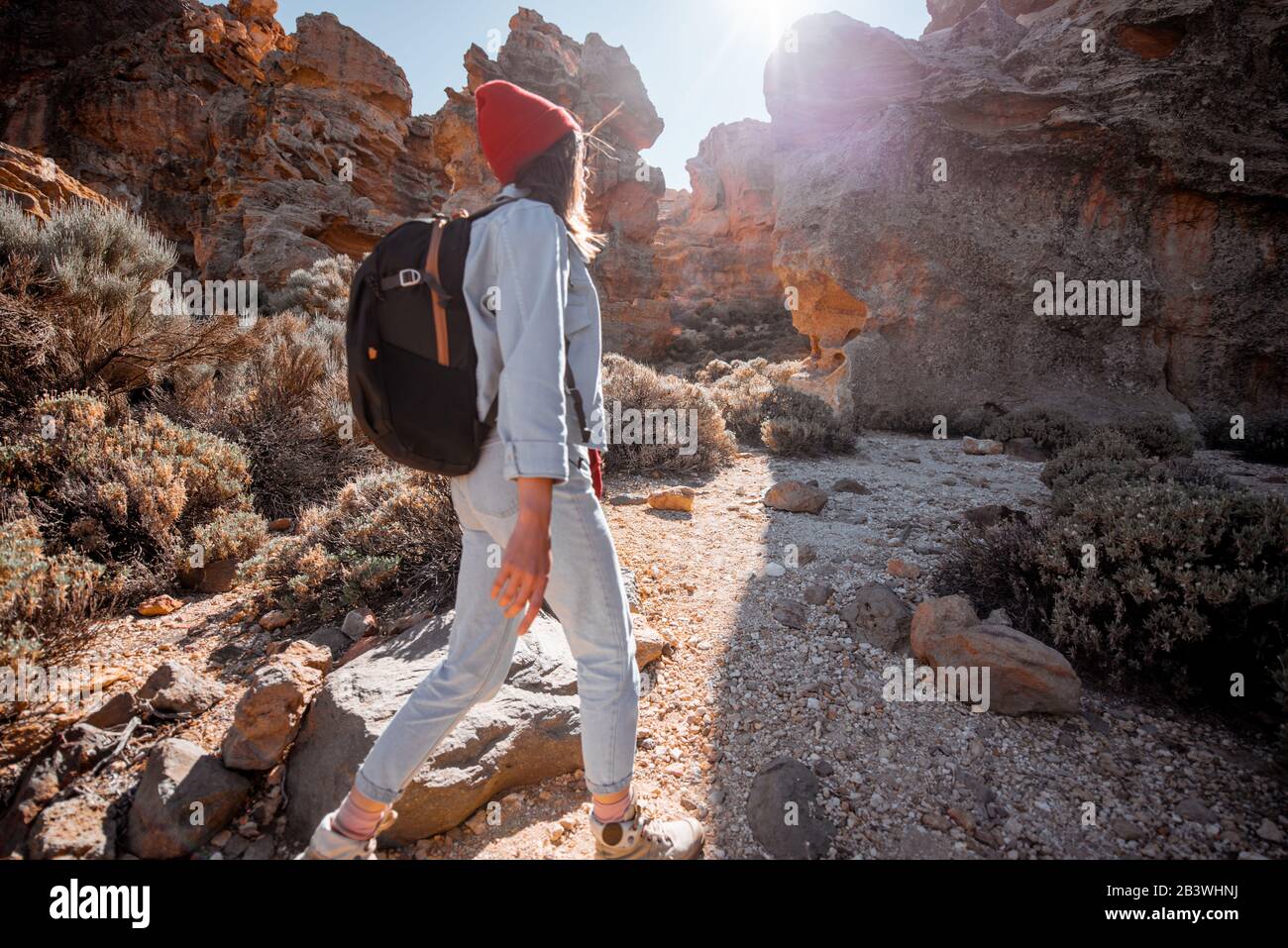 Young female traveler walking on the rocky terrain between huge rocks volcanic origin during a sunny day. Image focused on the background, woman is out of focus Stock Photo