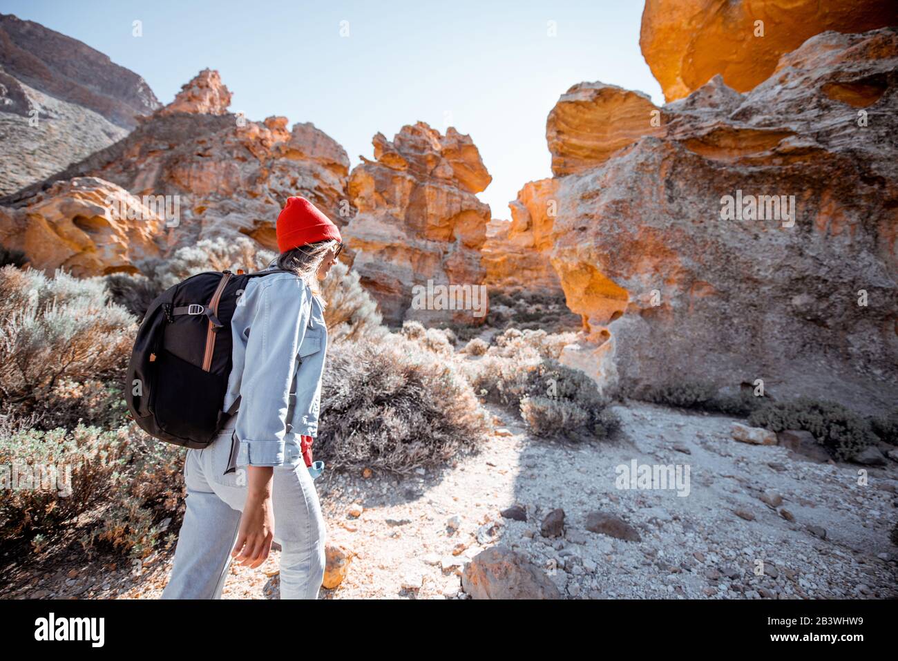 Young female traveler walking on the rocky terrain between huge rocks volcanic origin during a sunny day. Traveling on Tenerife island, Spain Stock Photo