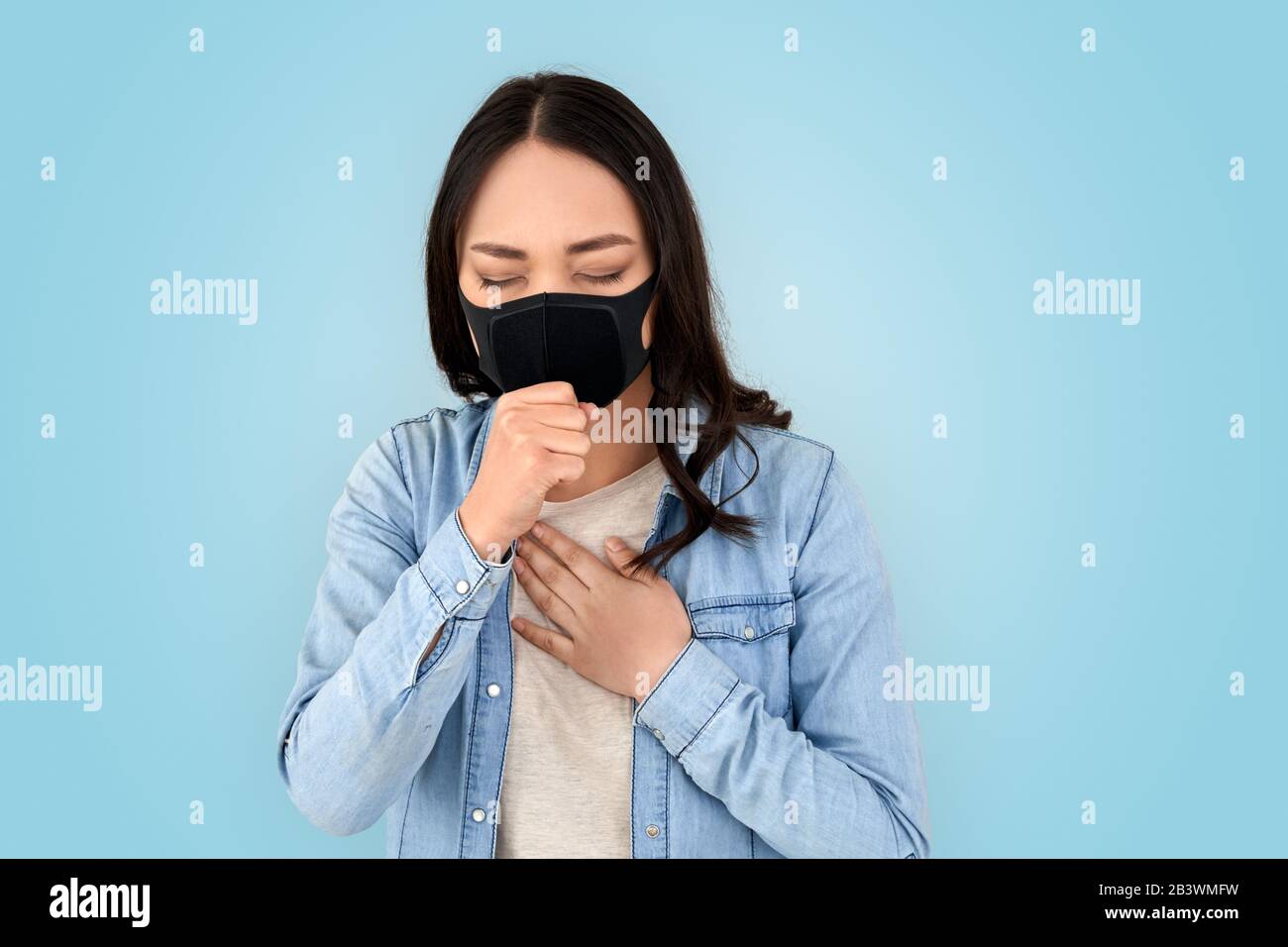 Coronavirus Concept. Chinese woman in respirator mask standing isolated on grey coughing concerned Stock Photo