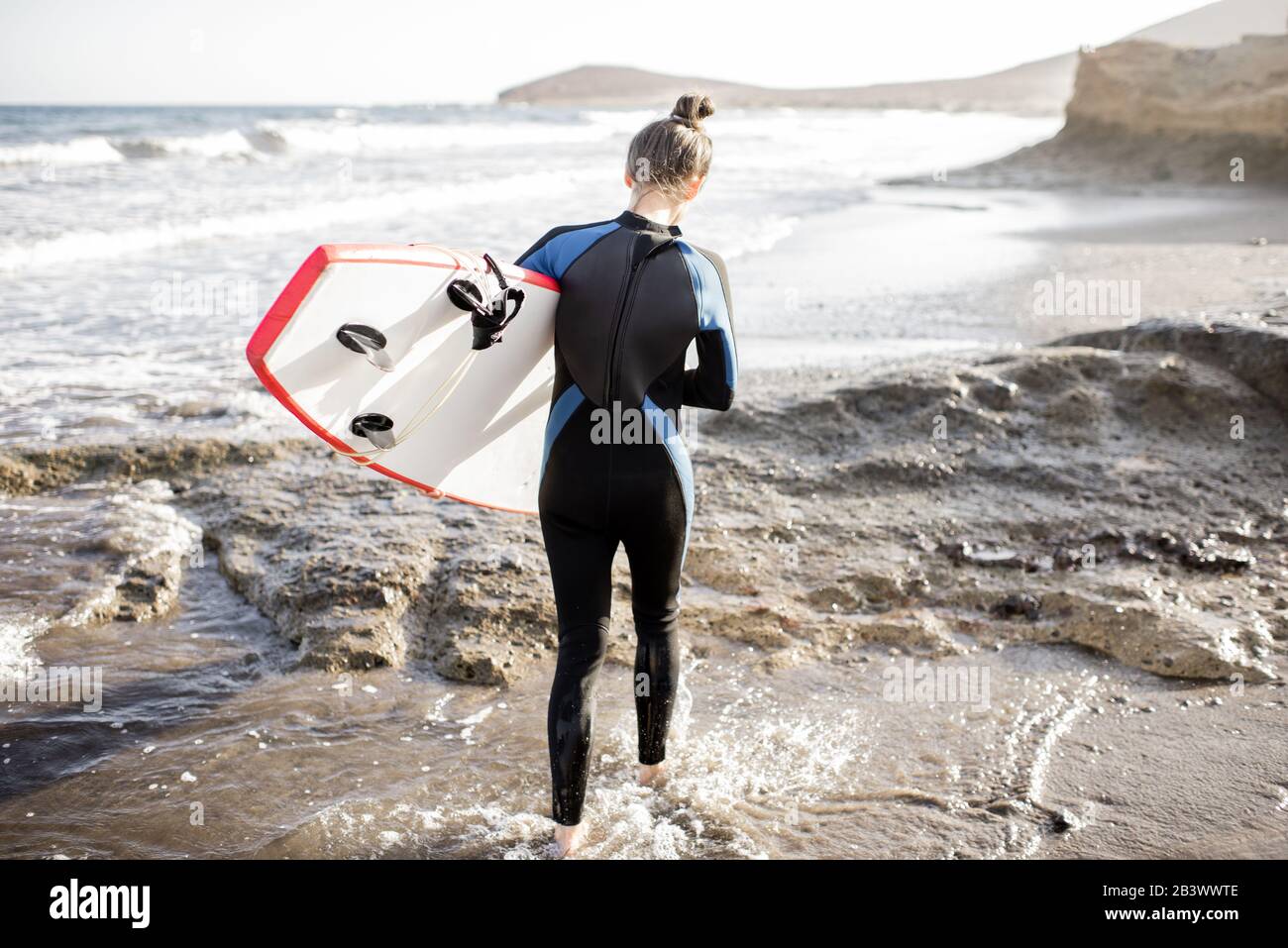 Young woman in wetsuit walking with surfboard on the beautiful wild